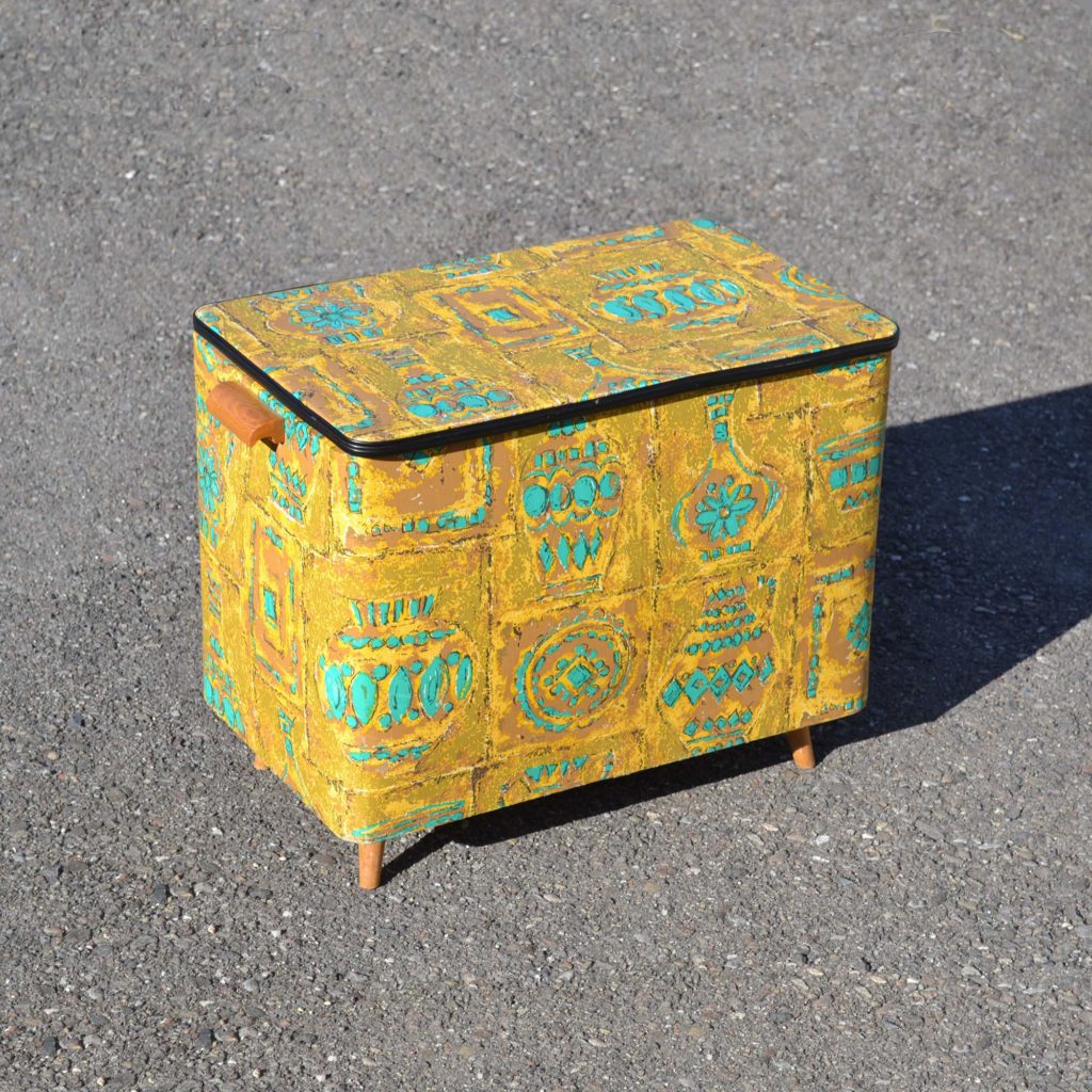 Coffre à jouets des années 1960, avec habillage en vinyle imprimé décor sixties. Avec couvercle pivotant. couleur moutarde et turquoise.
