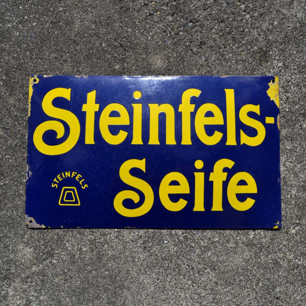 Plaque émaillée pour le savon Steinfels. D’origine Suisse alémanique. Bombée, vers 1910-20. Fond bleu, avec lettrage jaune. Schweizer Emailschild.