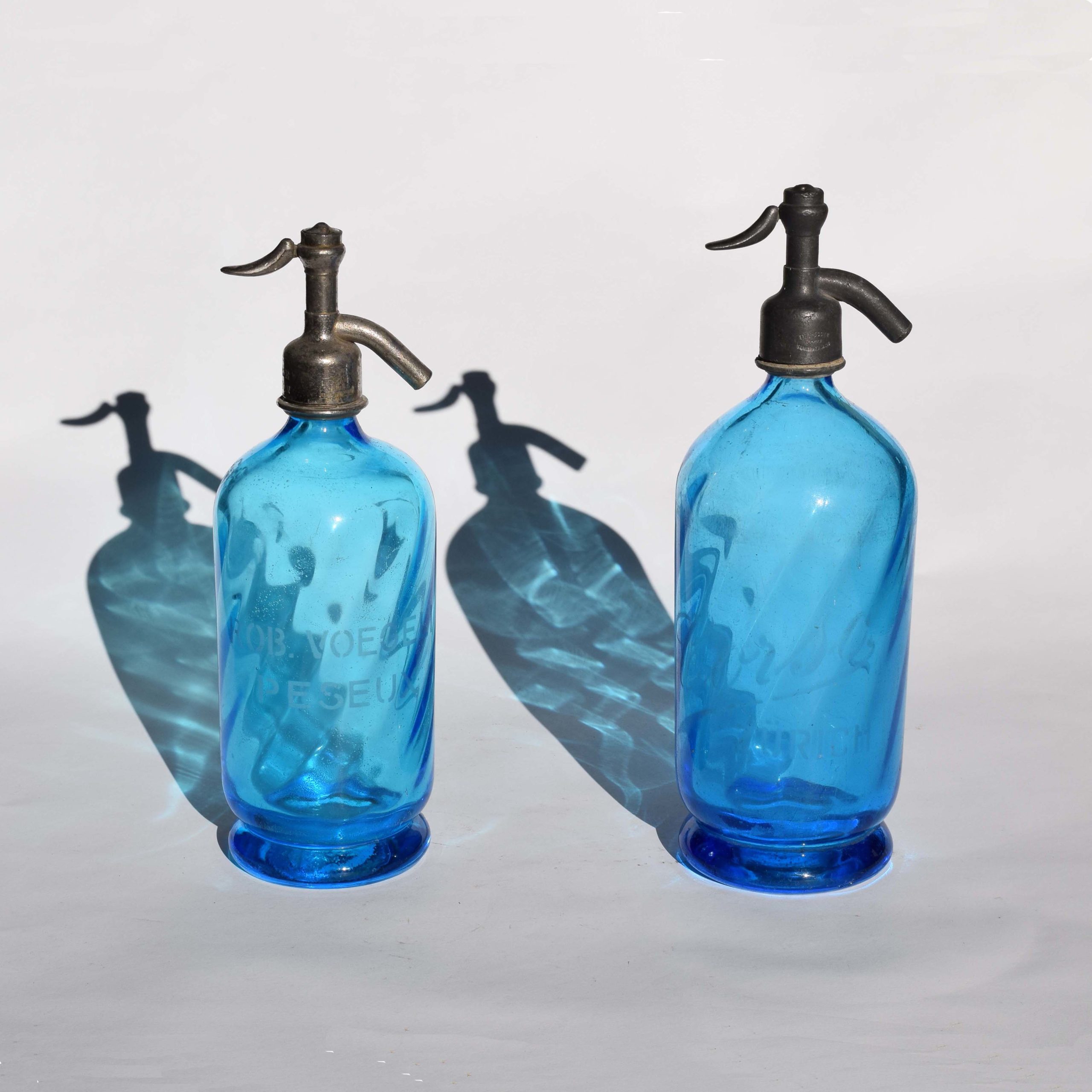 Anciens siphons à eau de Seltz en verre avec belle couleur bleu, d’origine Suisse : A gauche marquage Robert Voegeli Peseux. A droite, un peu plus gros, marquage Corso Zurich.