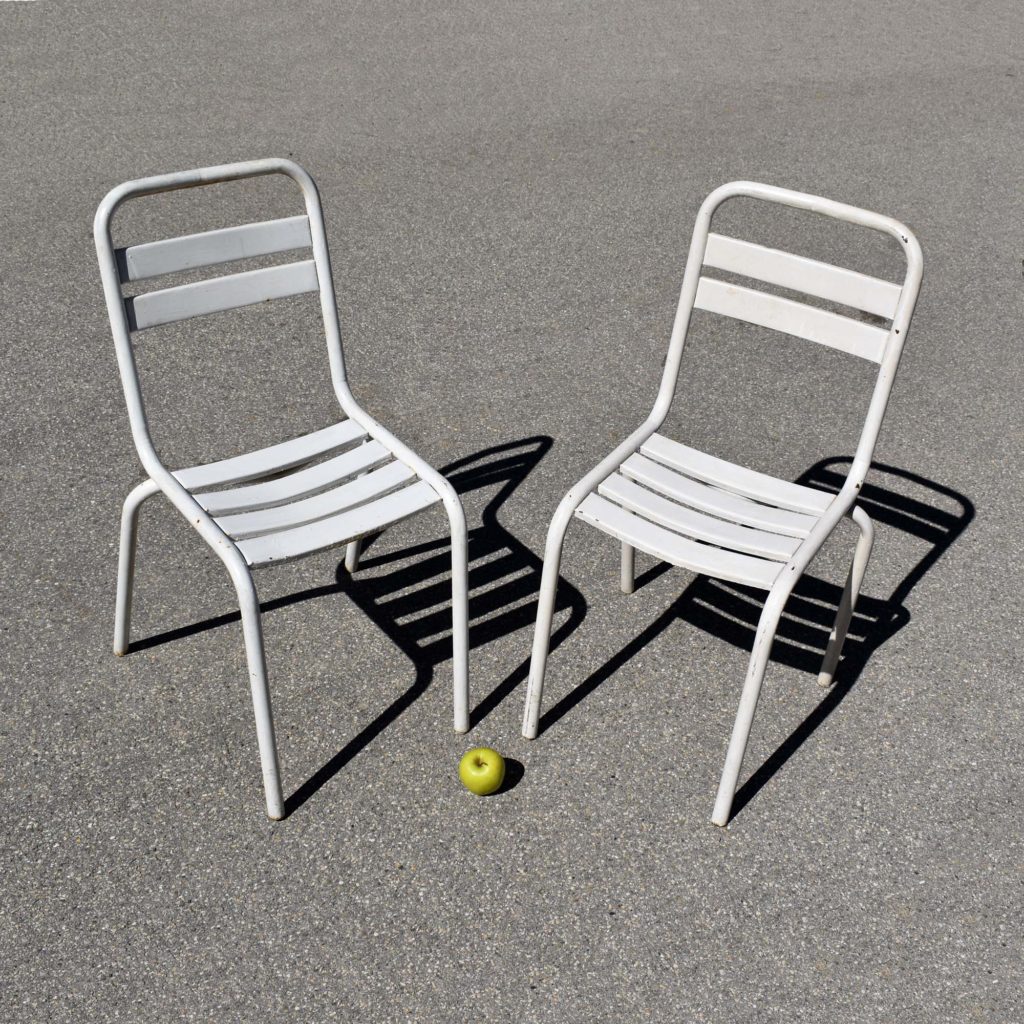 Lot de 2 chaises de jardin métalliques, avec peinture blanche d’origine. Peut-être du label Tolix, modèle “T2”. Châssis tubulaire, avec lattes en tôle emboutie.