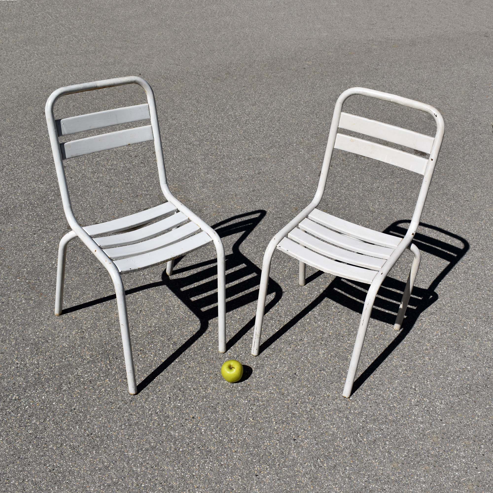 Lot de 2 chaises de jardin métalliques, avec peinture blanche d’origine. Peut-être du label Tolix, modèle “T2”. Châssis tubulaire, avec lattes en tôle emboutie.