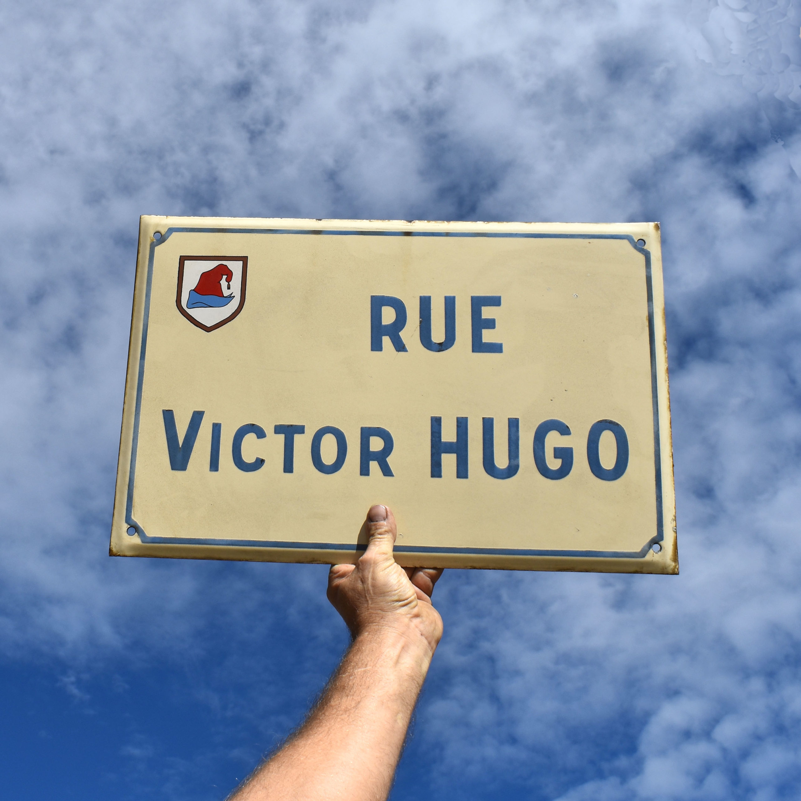 Plaque de rue émaillée française. Rue Victor Hugo. Avec fond beige et lettrage bleu. Blason de la ville de Guebviller.