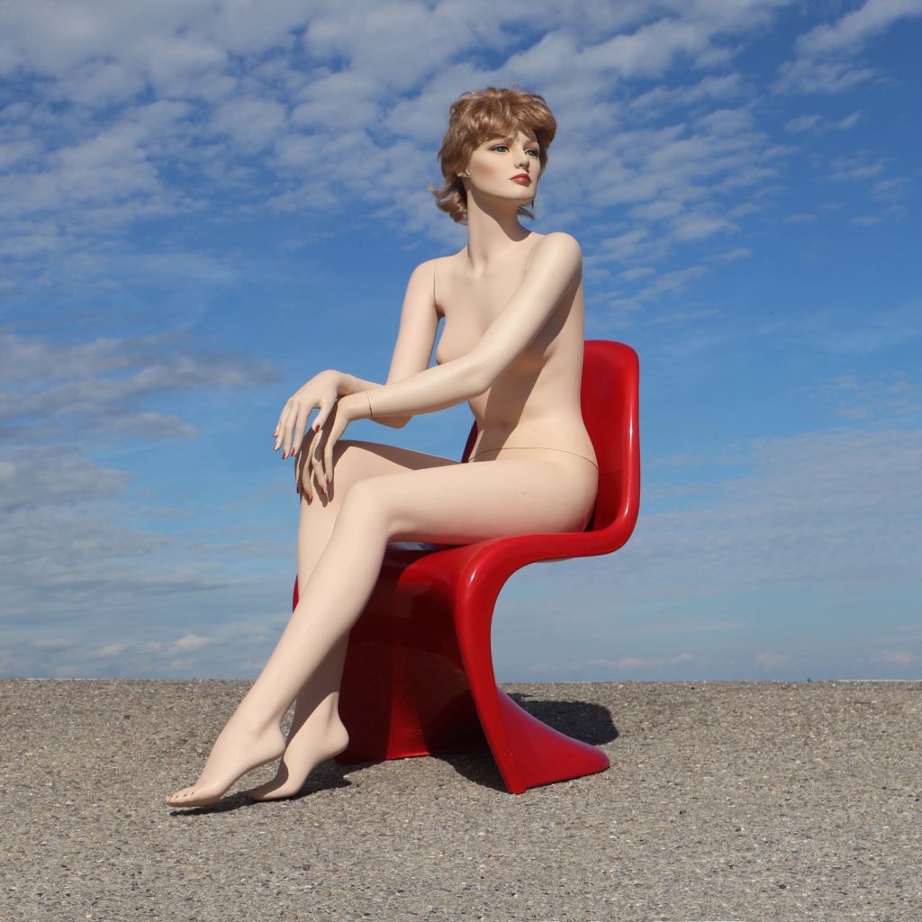 Mannequin de vitrine en position assise bras croisés sur les jambes. Mannequin de boutique vintage des années 1990, couleur chair clair. Maquillée, avec perruque.