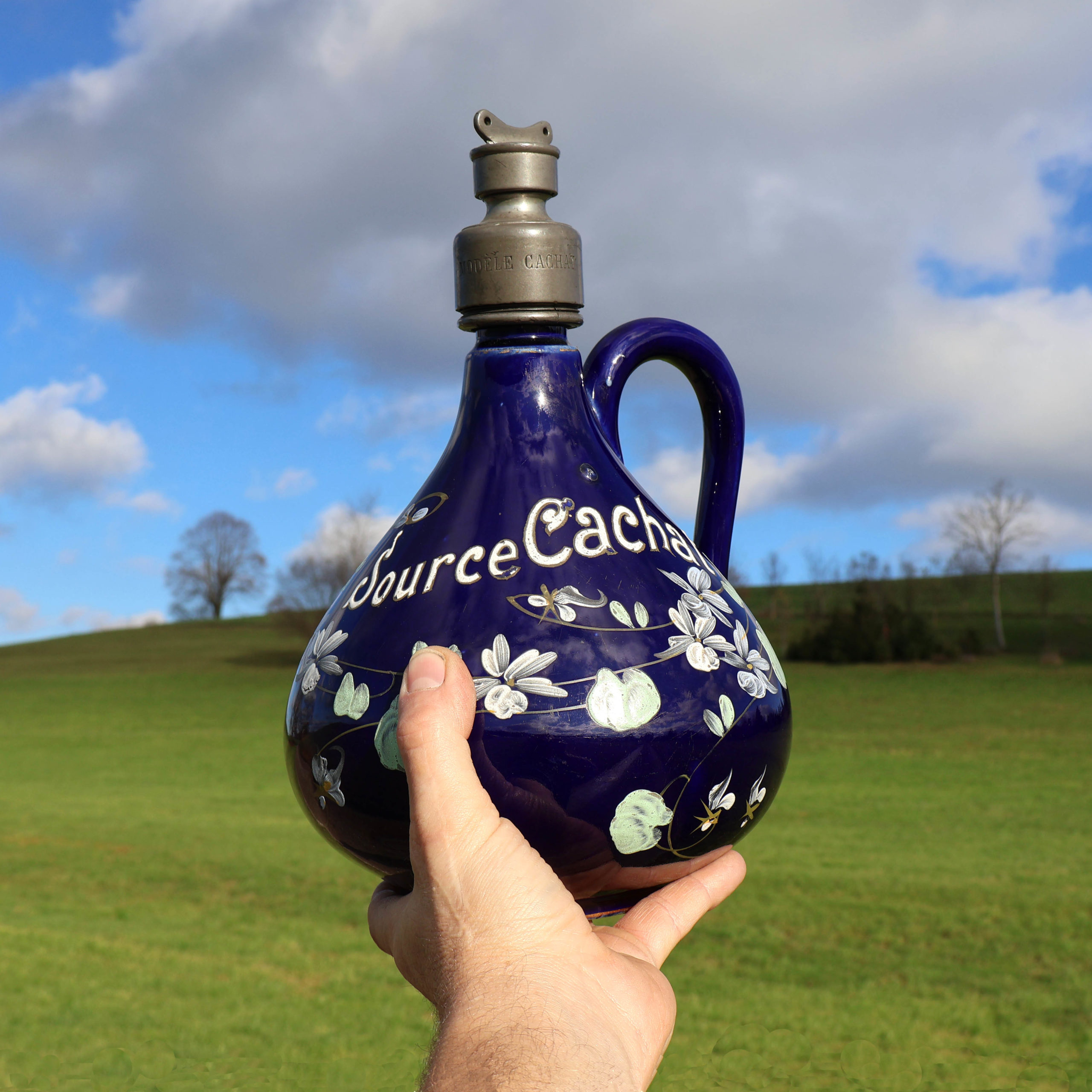 ancienne cruche en faïence émaillée 1900 de la source Cachat à Évian. Objet publicitaire de curiste. Flacon avec émaillage bleu cobalt, décor floral et lettrage source Cachat.