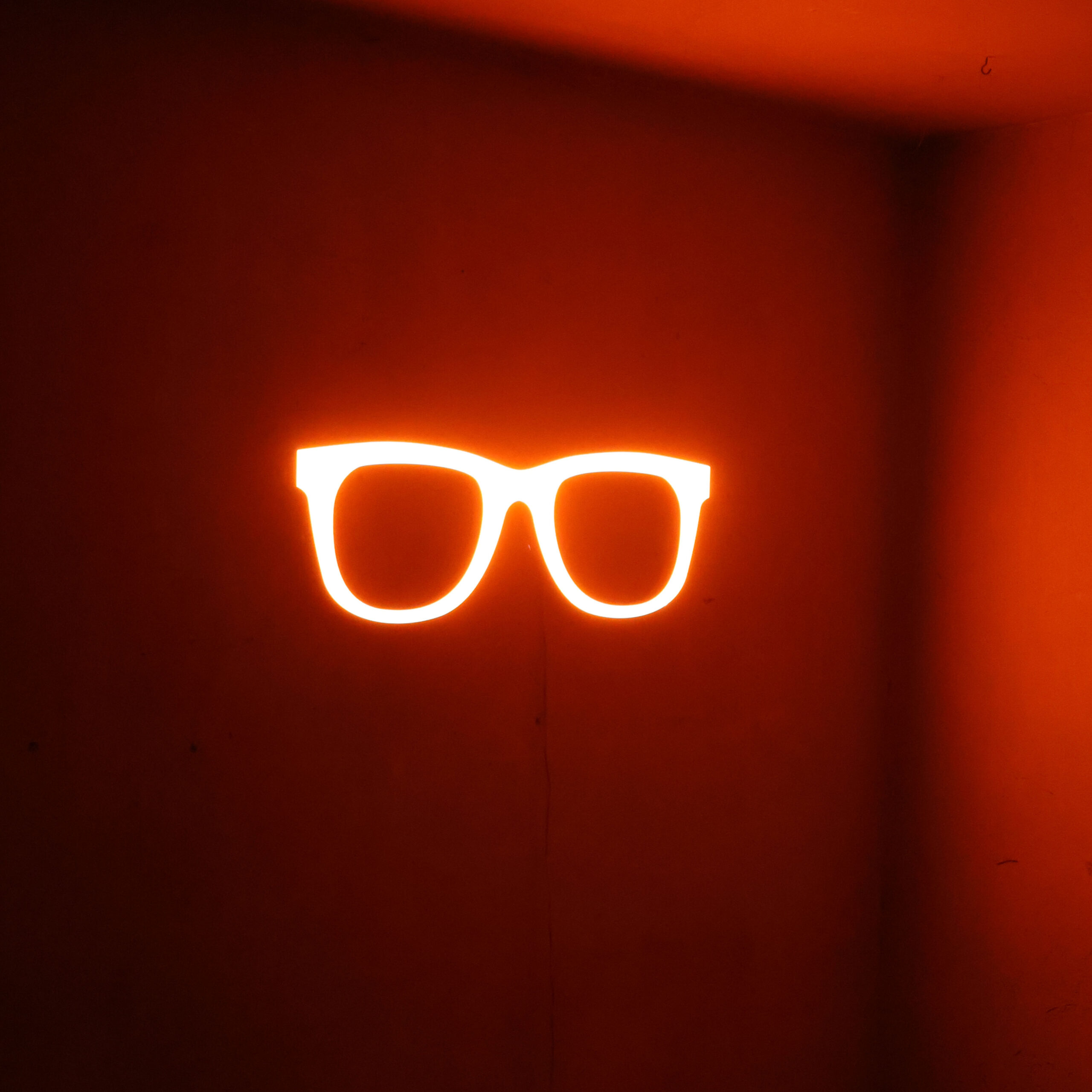 Enseigne lumineuse d'opticien, en forme de paire de lunettes, en 3D. Modèle d'occasion en plastique orange, illuminée en LED. Déco murale insolite.